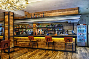 Frontal de la barra con sillas altas y botellas - Massé Drinks & Pool